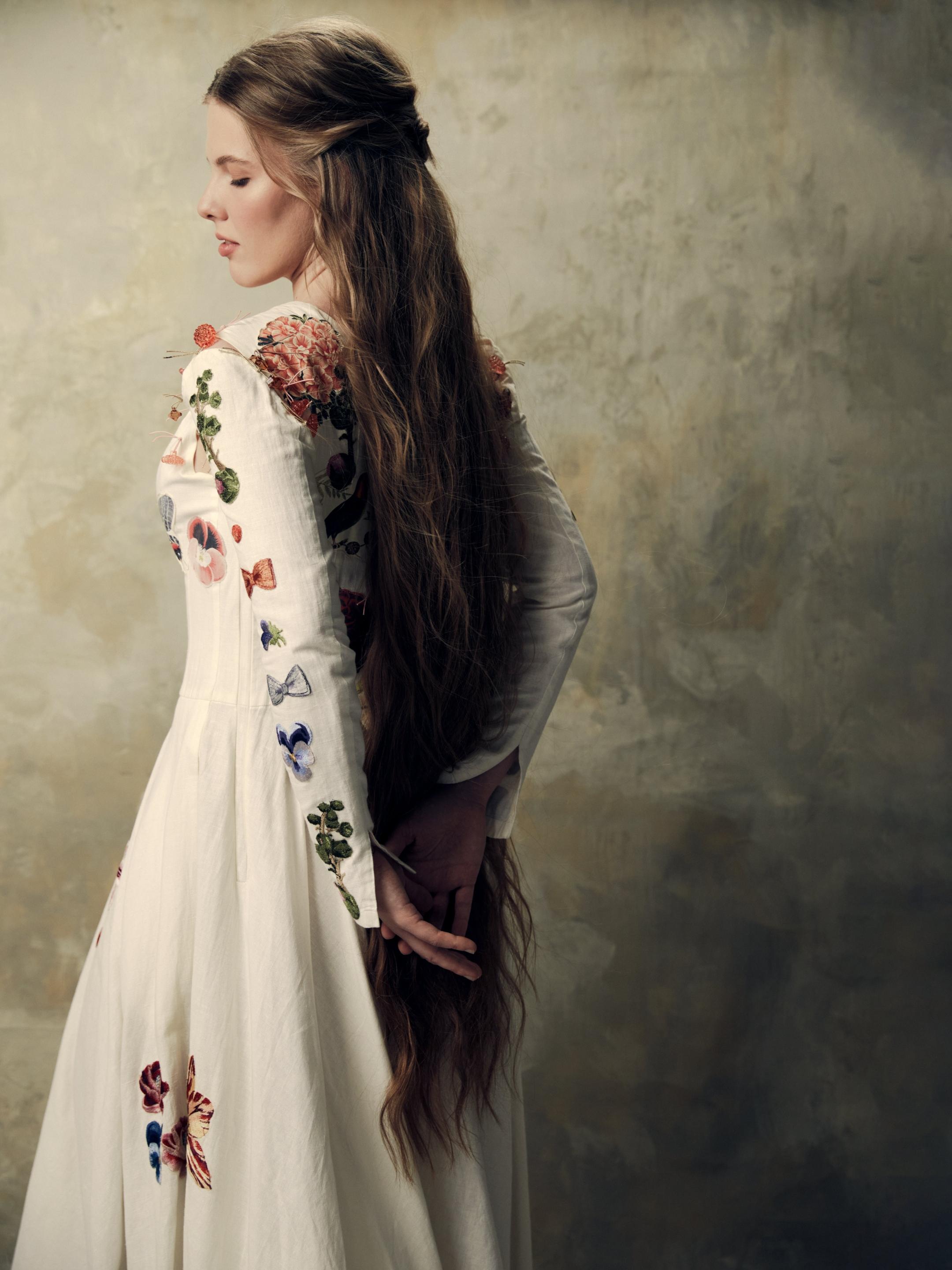 Eva Gevorgyan Frau mit langen Haaren in einem langen weißen Kleid mit Blumenverzierung.