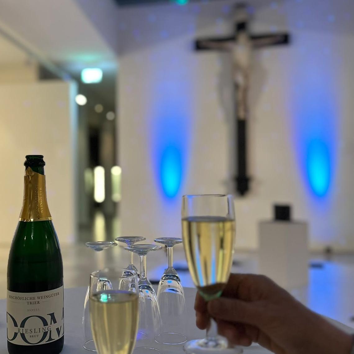 Sekt im Innenraum des Museums am Dom mit Kreuz und blauer Beleuchtung im Hintergrund.