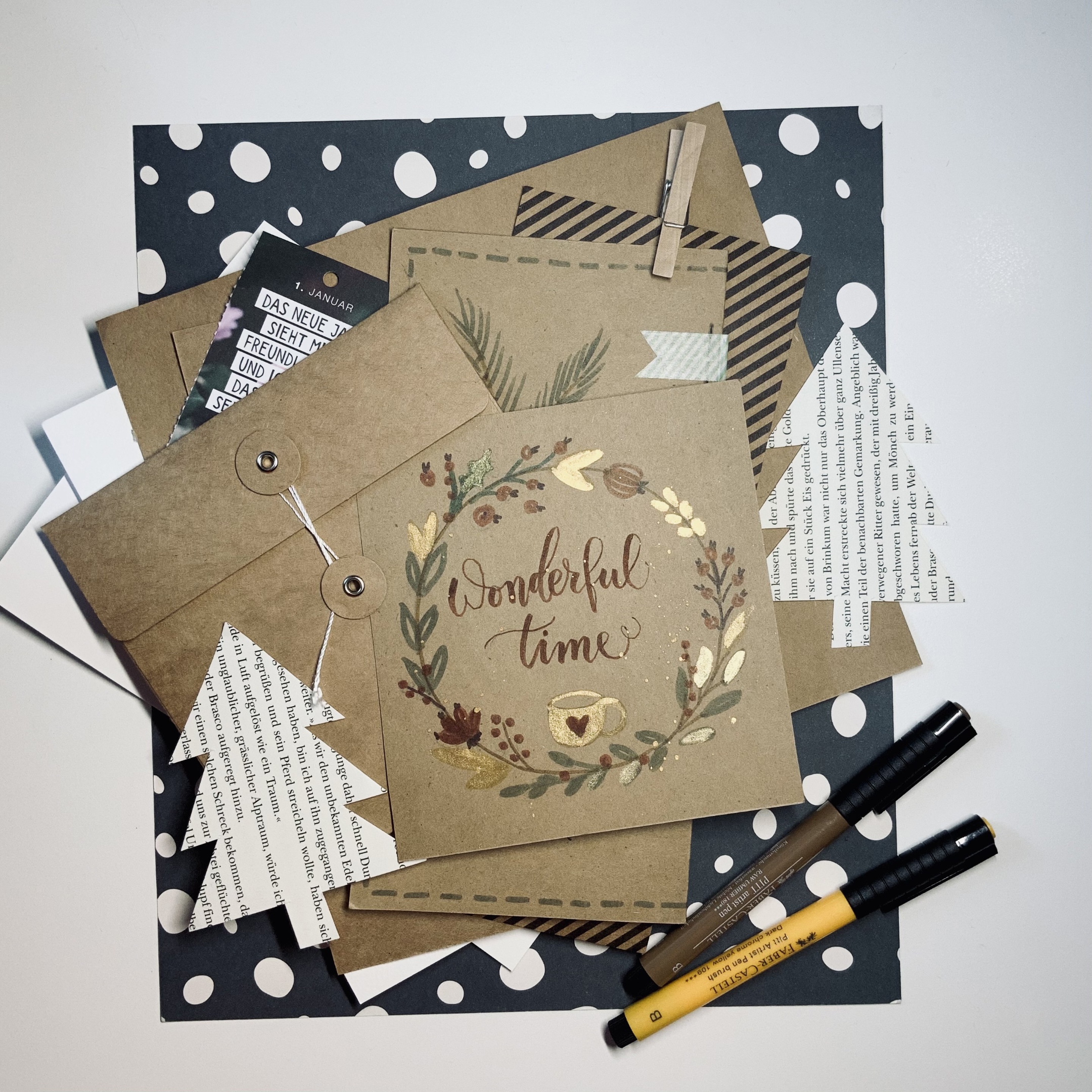 Kalligraphie Stifte liegen auf gepunktetem Papier. Es liegen viele verschiedene Karten und Umschläge aufeinander zusammen mit ausgeschnittenen Weihnachtsbäumen aus Papier. Auf der obersten Karte steht 'Wonderful Time'.