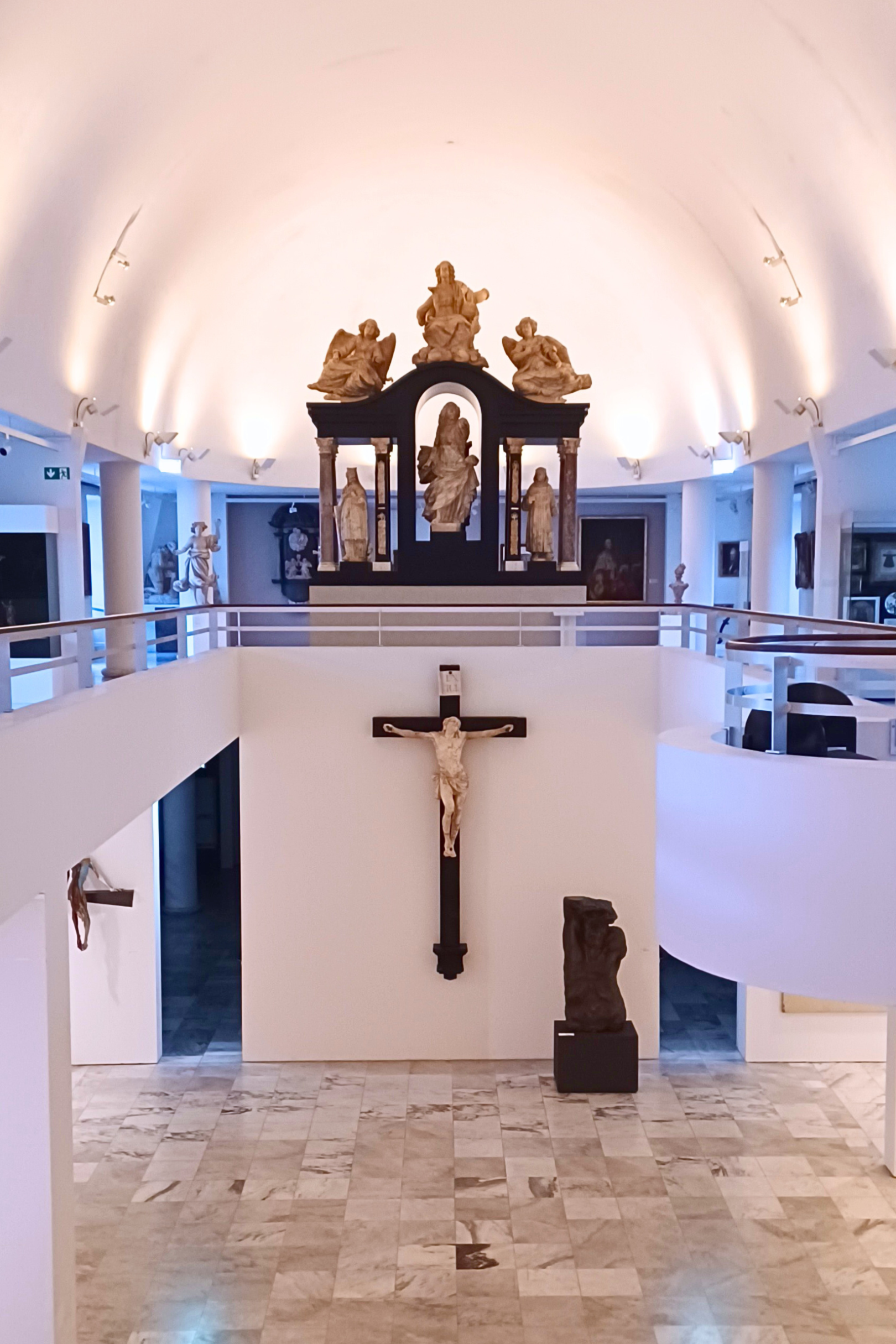 Ausstellungsraum für christliche Kunst mit Kruzifix und religiösen Skulpturen in modern beleuchtetem Museum.