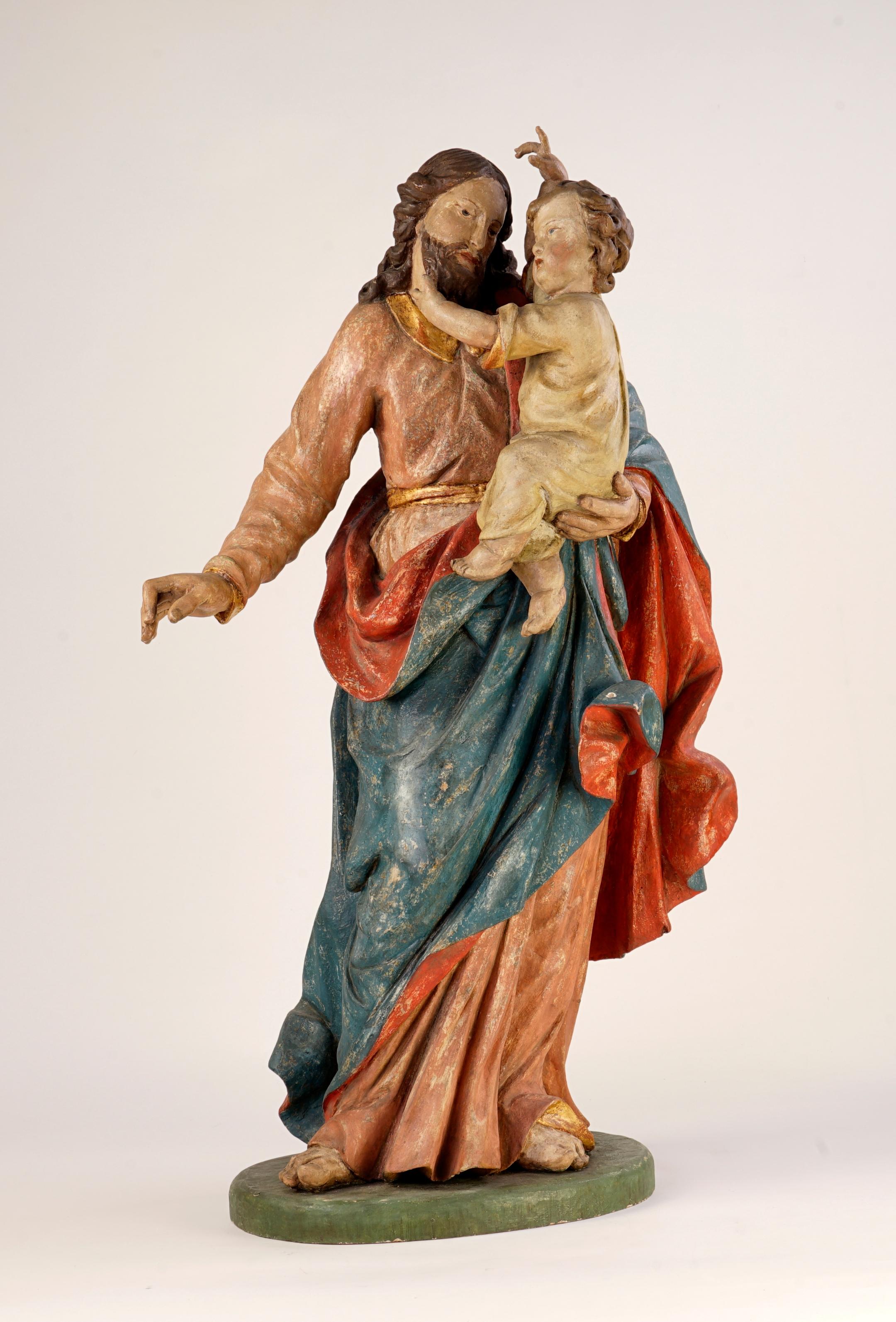 Josef, der Verlobte von Maria, hält das kleine Jesuskind auf dem Arm.